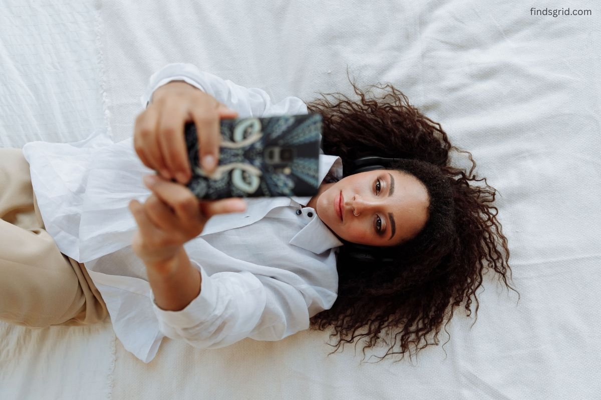 Woman lying on her back holding a phone above her face in bed