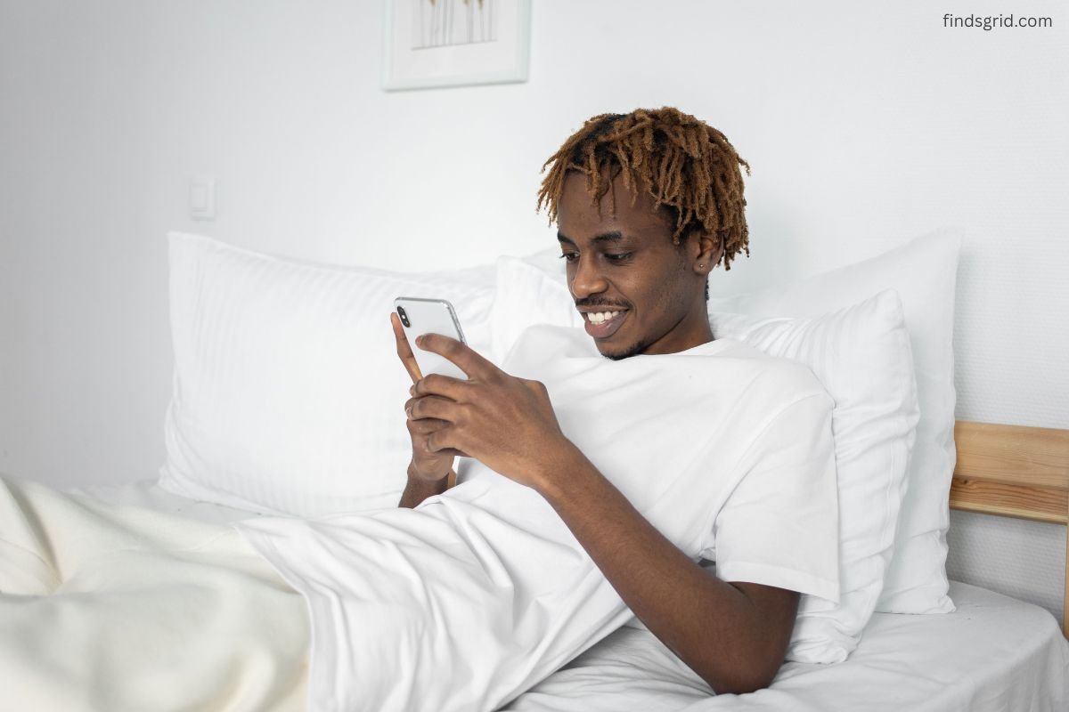 Man propped on stacked pillows with chin tucked while scrolling his phone in bed